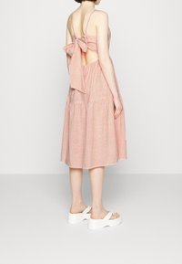 Punainen ja valkoinen raidoitettu midi-mekko, jossa avonainen selkä, solmittu nauhatyyny ja kerroksellinen hame. Yhdistetty valkoisiin platform-sandaaleihin.