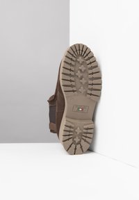 Botte en daim marron avec une semelle en caoutchouc beige présentant un motif de semelle texturé et antidérapant. Inclut une étiquette de marque indiquant un savoir-faire italien.
