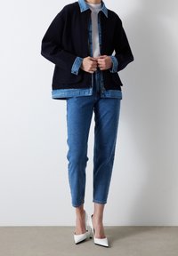 Černá bunda s džínovým límcem a manžetami, vrstvená přes bílý top. Párek světle modrých džín a bílé lodičky s špičatou špičkou.