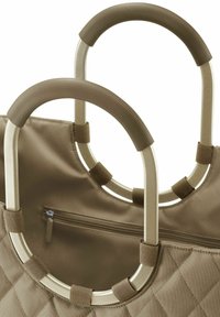 La bolsa tote acolchada beige cuenta con dos asas de metal con empuñaduras texturizadas. Incluye un bolsillo con cremallera para un almacenamiento seguro.