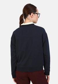 Felpa blu navy con colletto e polsini a coste, caratterizzata da una cucitura orizzontale sul retro e una vestibilità rilassata. Il materiale sembra morbido.