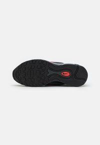 Black athletic shoe sole with textured rubber for grip, featuring a prominent red logo detail and a wave-like tread design.