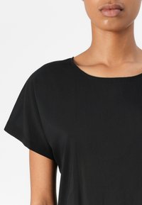 Haut noir à manches courtes avec un col rond et un tissu lisse et léger. Design simple avec un minimum de coutures visibles.