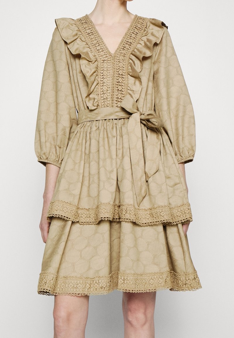 Robe beige avec un col en V, un col volanté et des manches ballon. Caractéristiques d'un tissu texturé, d'un design à étages et de détails en dentelle à l'ourlet.