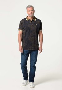 Zwarte poloshirt met een gouden abstract patroon, voorzien van een bruine kraag en afwerking. Gekocht met blauwe jeans en witte sneakers.