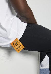 Black pants with an orange label showing "240gsm" attached to a white t-shirt, creating a contrast between colors and textures.