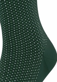 Grüne Socke aus strukturiertem Strickmaterial, mit einem Muster aus kleinen weißen Punkten. Runde Zehenpartie und verstärktes Fersenbereich.