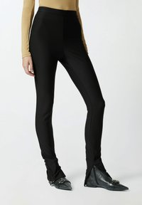 Crne tajice s visokim pojasom, s uskim dizajnom i bočnim patentnim zatvaračima na gležnjevima. Uparene s crnim cipelama na visoku petu s oštrom tobom.