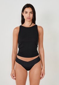 Top nero senza maniche realizzato in tessuto liscio, abbinato a slip neri da bikini brillanti con vita a forma di V.
