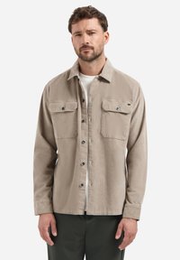Light taupe button-up shirt made of textured fabric with two chest pockets and a collared neckline, paired with a white undershirt.