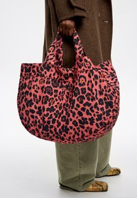 Duża torba typu tote w różowym materiale z czarnym wzorem w cętki lamparta. Posiada podwójne, solidne uchwyty oraz zaokrąglony kształt, odpowiednia do różnorodnych zastosowań.