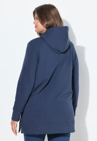 Tmavě modrá mikina s kapucí, dlouhými rukávy, volným střihem a bočními rozparky na lemu. Vyrobena z měkké, strukturované tkaniny.