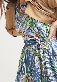 Robe fleurie avec un imprimé vibrant de feuilles bleues et de fleurs multicolores. La taille est accentuée par une ceinture à nouer assortie.