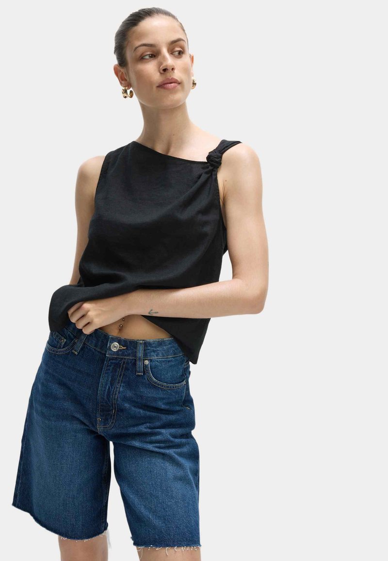 Top nero senza maniche con dettaglio annodato sulla spalla, abbinato a pantaloni shorts in denim blu con orli sfrangiati e design classico a cinque tasche.