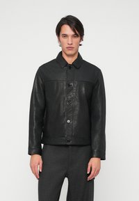 Casaco de couro preto com colarinho, fecho frontal por botões e uma textura suave. Apresenta uma costura horizontal ao longo do peito.