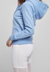 Ljusblå hoodie med foder i huva, ribbade ärmslut och nederkant. Bärs med vita tajta shorts. Mjuk tygkvalitet och avslappnad passform.