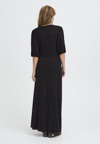 Rochie maxi neagră, realizată dintr-un material elastic, cu un corp strâns, mâneci bufante și o fustă fluidă care se extinde până la glezne.