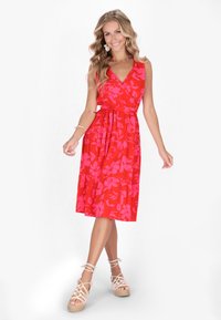 Rotes Blumenkleid mit Wickeldesign, V-Ausschnitt, Taillenkordel und gestuftem Rock. Das Material wirkt leicht und fließend, entworfen für eine bequeme Passform.