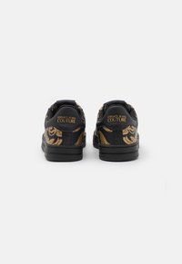 Černé sneakers s pozlaceným ornamentálním vzorem, s hladkým povrchem a polstrovaným límcem. Logo je vyražené na patě. Gumová podrážka.