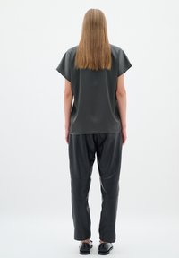 Top gri, cu mânecă scurtă, din țesătură texturată; asociat cu pantaloni din piele negri și pantofi negri. Finisaj moale, mat, cu o croială lejeră.