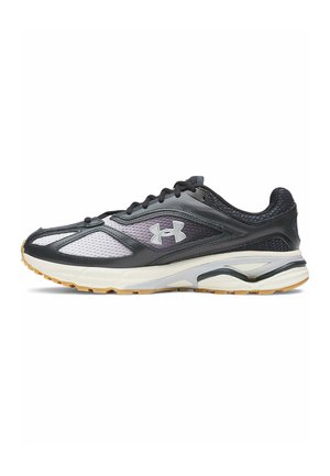 Zwart-witte Under Armour hardloopschoen met mesh panelen, gewatteerde zool en buitenzool van rubber, gezien van opzij.