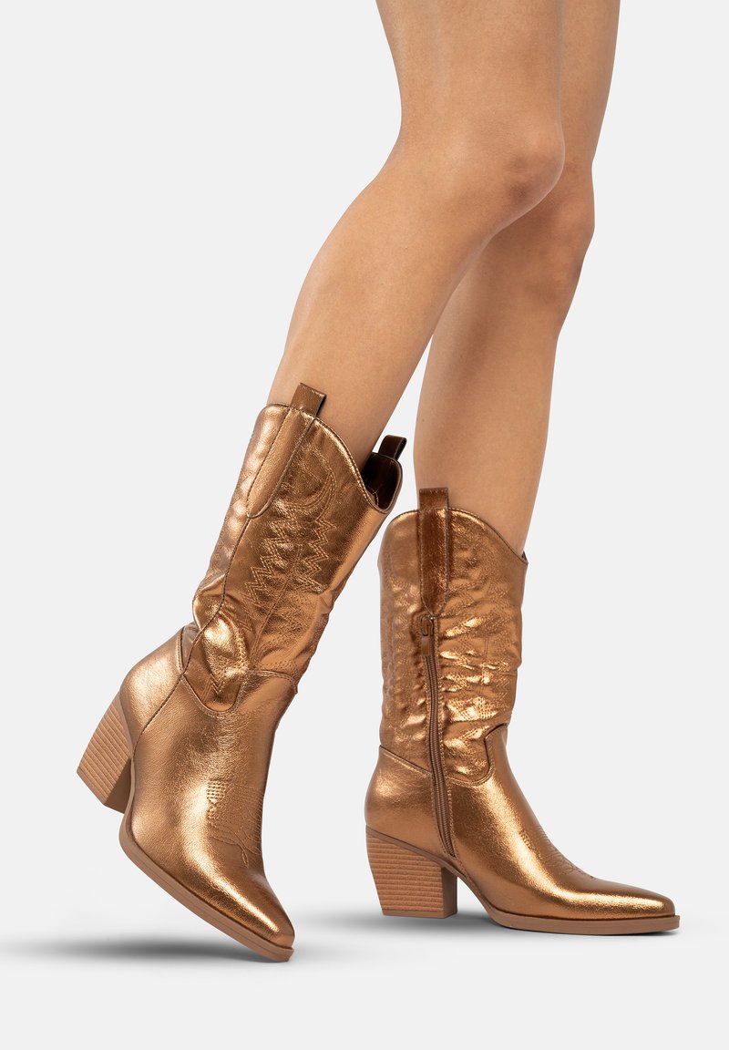 Botas de vaquero de bronce con un acabado texturizado, punta afilada y tacón cuadrado. Presentan una cremallera lateral y costuras decorativas en el caña.