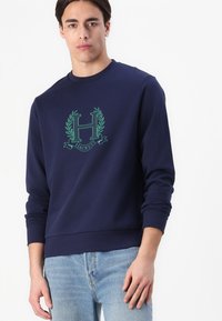 Navy blue sweatshirt featuring a green embroidered "H" logo with laurel accents, round neckline, and ribbed cuffs and hem. Casual fit.