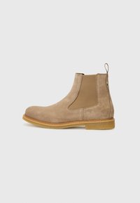 Bottines Chelsea en daim beige avec des panneaux élastiques sur les côtés, bout arrondi et semelle en caoutchouc beige. Dotées d'une languette pour un enfilage facile.