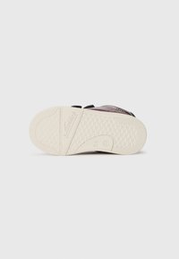 Schwarzer Schuh mit Muster, weichem Obermaterial aus Stoff und Klettverschlüssen. Die weiße Gummisohle verfügt über strukturierte Grifdetails und das Markenlogo.