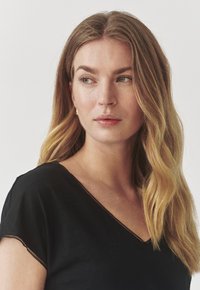 Maglietta nera a scollo a V con maniche corte, caratterizzata da un bordo testurizzato lungo il collo. Il tessuto sembra morbido, adatto per un abbigliamento casual.