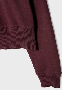 Pull en maille à manches longues couleur bordeaux foncé avec poignets et ourlet côtelés visibles sur fond gris clair.