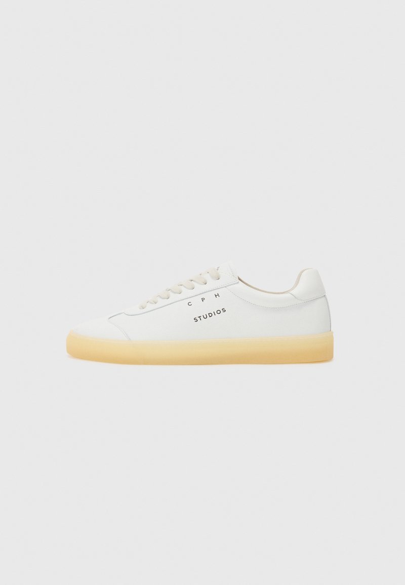 Adidași albi cu un upper din piele netedă, bot rotund și accente bej. Prezintă logo-ul "CPH STUDIOS" și o talpă din cauciuc maro deschis.