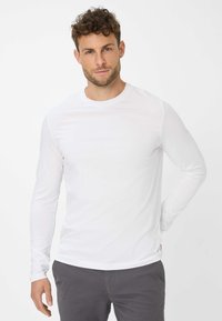 Langærmet crewneck t-shirt i hvid, lavet af glat bomuld. Har et figursyet design og subtile syninger, båret med mørkegrå bukser.