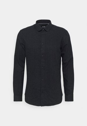 Camisa de manga larga oscura, con botones, hecha de una tela texturizada, que presenta un cuello clásico, botones en la parte delantera y un dobladillo curvado.