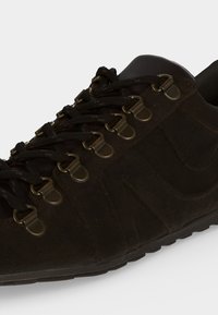 Chaussure de marche marron foncé avec œillets métalliques en forme de D et lacets noirs, dessus en cuir finement travaillé et semelle en caoutchouc visible en dessous.