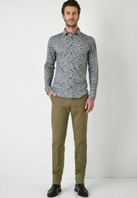 Gemusterte button-up Bluse in Marineblau, mit filigranen Blumenmustern, kombiniert mit hellbraunen Hosen und schwarzen Schuhen.