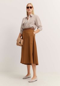 Weiß und braun gestreiftes Hemd mit Knöpfen, brauter gefälteter Rock, beiger Handtasche und hellen Ballerinas mit einem Netzmuster.