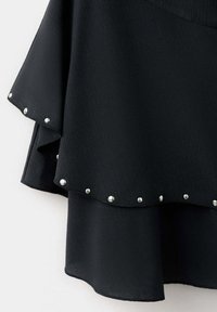 Tessuto nero con bordi sovrapposti adornati da piccoli borchie d'argento distribuite uniformemente su un indumento.