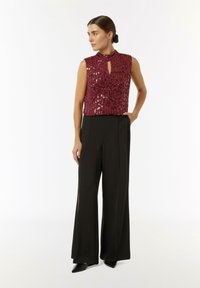 Burgunderfarbener ärmelloser Top mit Pailletten und Schlüssel-Ausschnitt, kombiniert mit hoch taillierten schwarzen weit geschnittenen Hosen. Schwarze spitze Schuhe runden den Look ab.