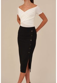 Svart pennkjol med en sidoklyvning och sex bruna knappar, tillsammans med en vit top med off-shoulder-design och vriden form.