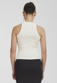 Top ajustado blanco sin mangas con un escote alto y amplias aberturas para los brazos. El material parece elástico y con relieve, destacando una textura suave.