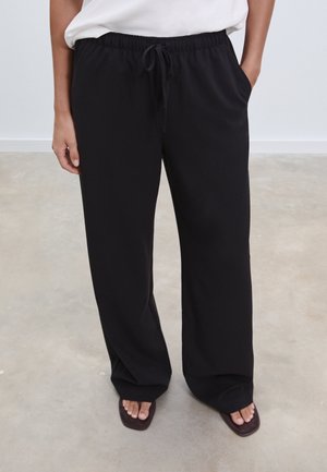 Pantalon noir à jambes larges en tissu doux avec une ceinture élastique et un cordon de serrage, doté de poches latérales et d'une coupe décontractée.