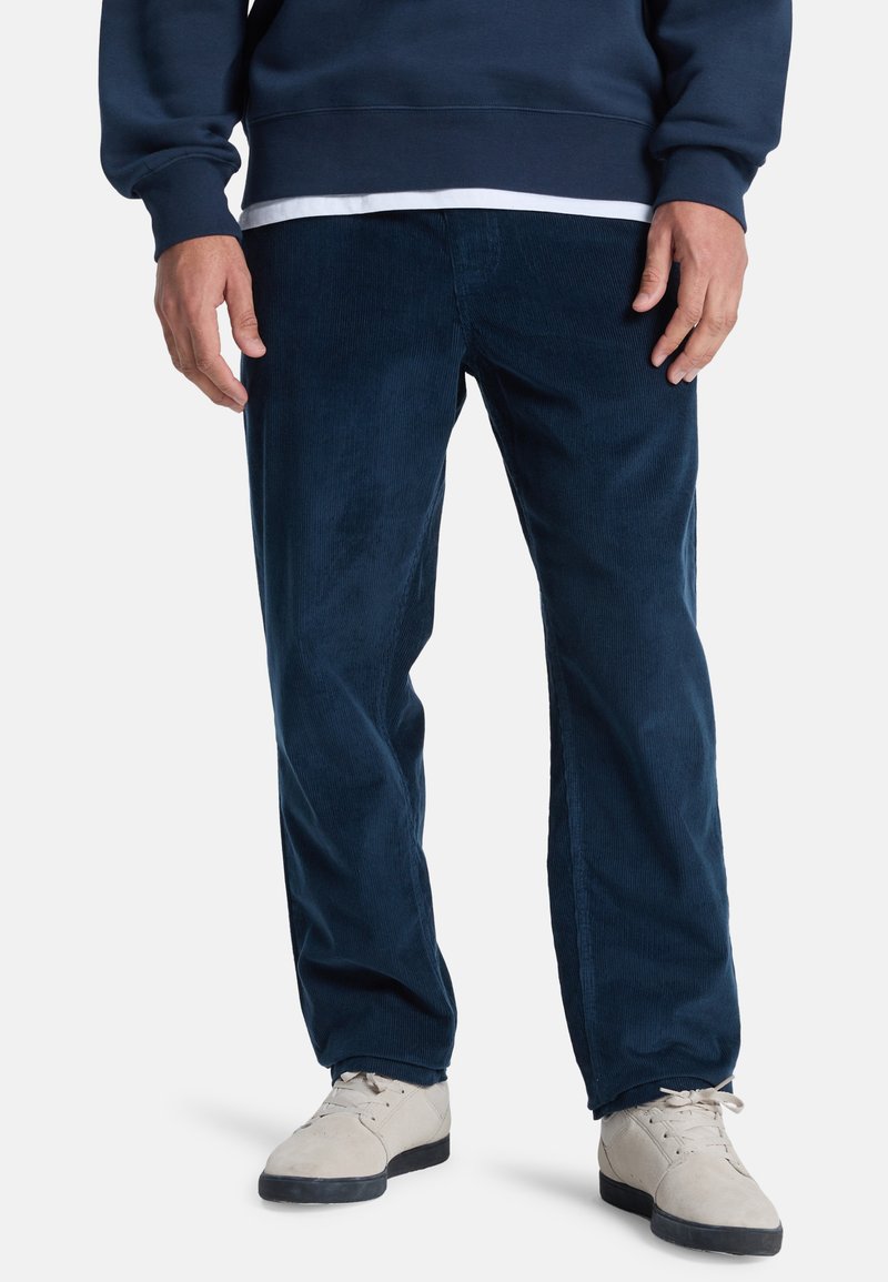 Navy corduroy broek met een rechte pasvorm, textuur oppervlak en zijzakken, gecombineerd met lichtgekleurde suède schoenen.