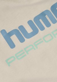 Cremefarvet stof med blå og mintgrøn tekst med ordene "human" og "PERFORMANCE." Teksten har en glat og mat struktur.
