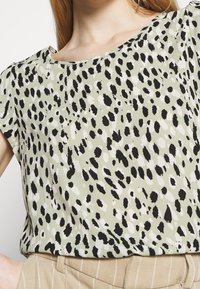 Blusa a maniche corte in tessuto verde chiaro con un motivo a pois bianco e nero. Texture liscia con una vestibilità comoda e scollatura ampia.