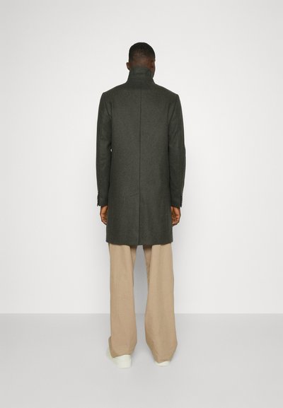 Gray wool coat with high collar, back vent, and tailored fit, paired with cream wide-leg trousers and white sneakers.