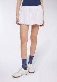 Minigonna plissettata bianca con vita elasticizzata, abbinata a sneakers bianche e calze a coste blu, caratterizzata da una superficie liscia.