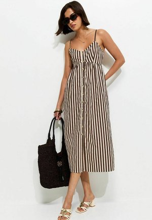 Femme portant une robe midi à boutons avec rayures verticales marron et blanches, des lunettes de soleil, des sandales à talons beiges, et tenant un grand sac fourre-tout tissé noir.
