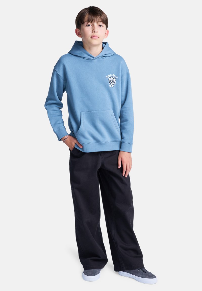 Felpa con cappuccio azzurro chiaro, dotata di tasca frontale e dettaglio con logo sul petto sinistro, abbinata a pantaloni neri a gamba larga e scarpe grigie.