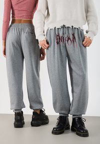 Grå sweatpants har en elastisk midje, sidelommer og en rød grafisk design. Bært med svarte snørebots for kontrast.